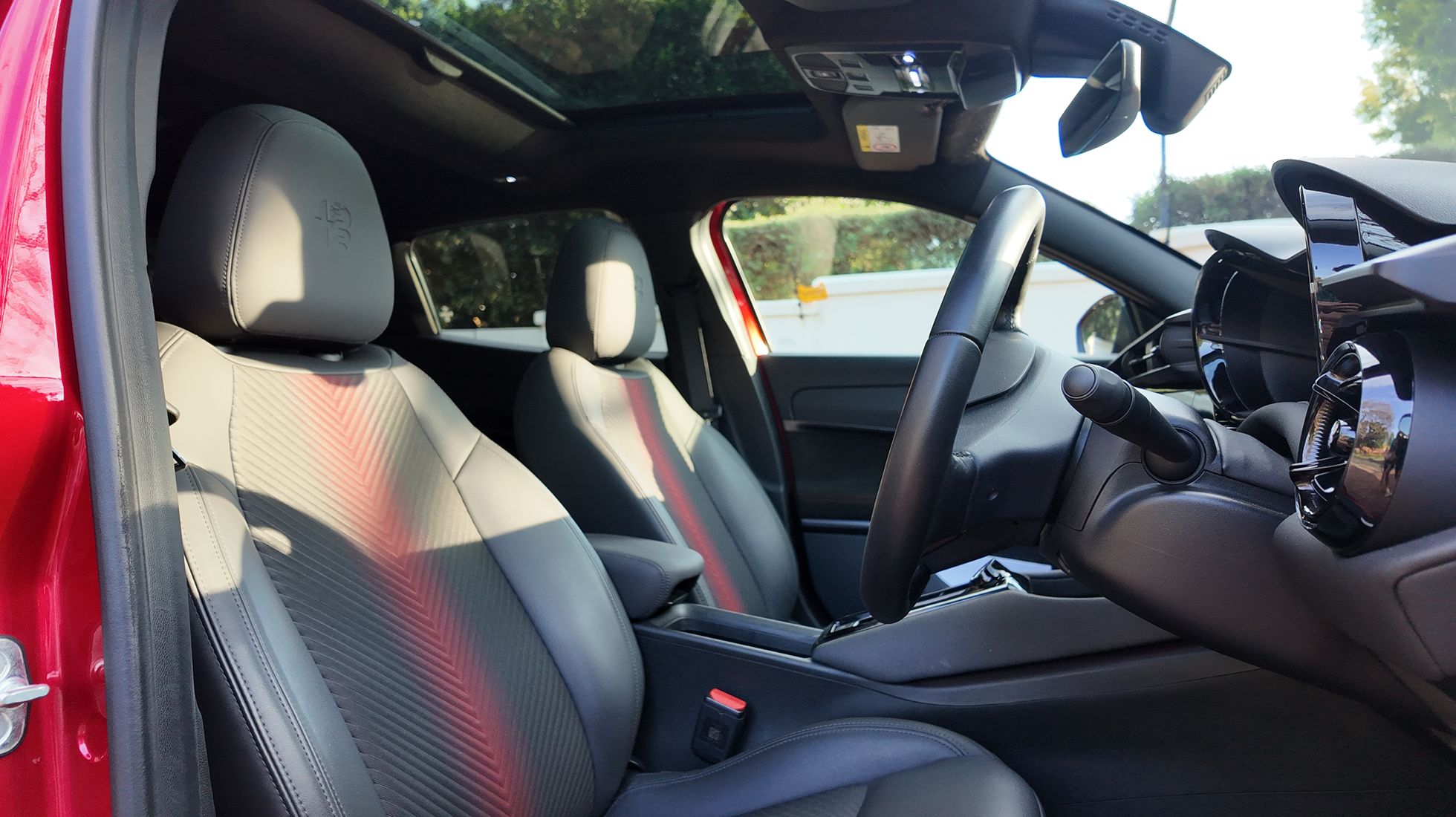 Front sports seats of the Alfa Romeo Junior Elettrica Veloce featuring black upholstery, red inserts and integrated headrests.