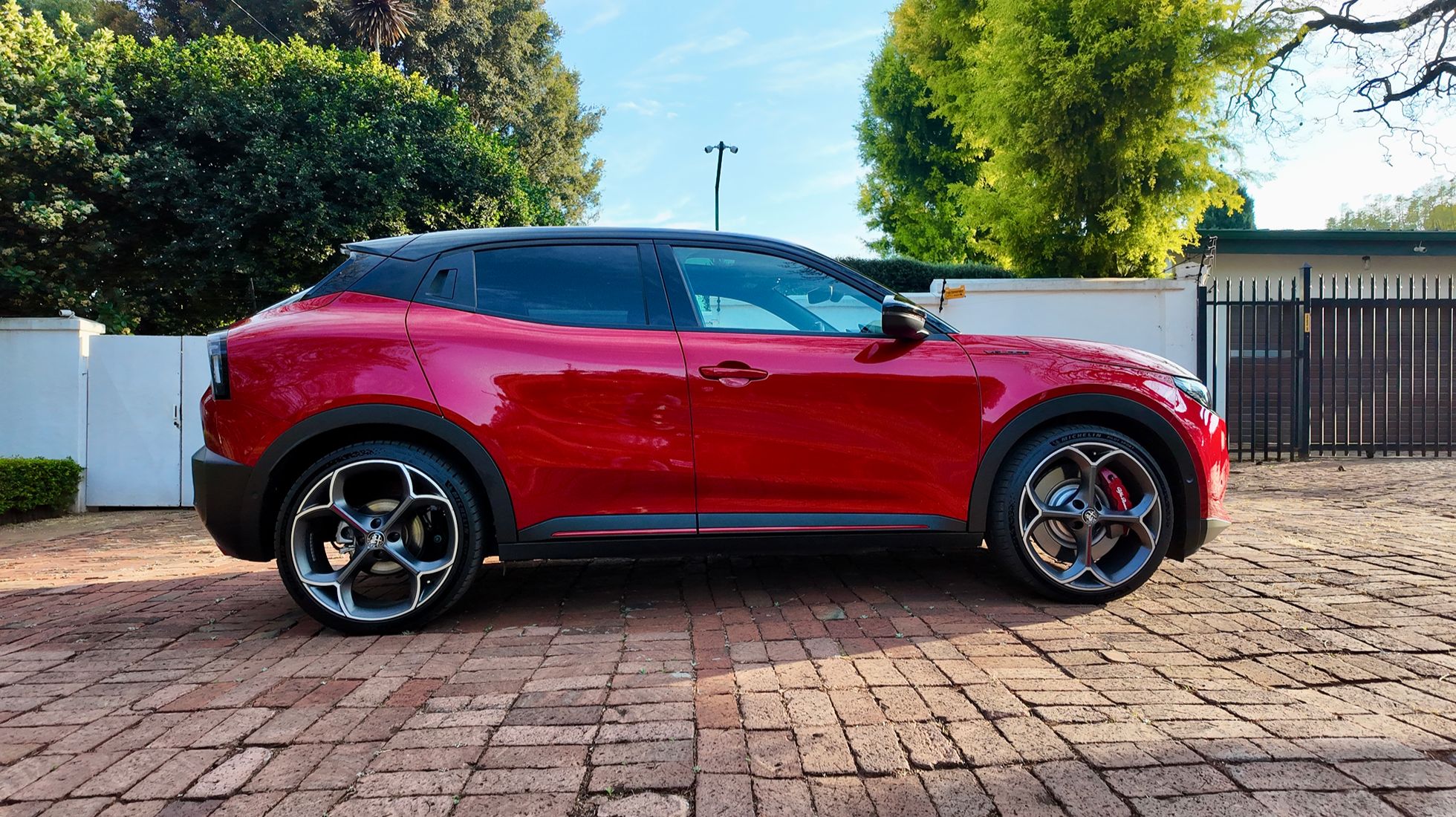 Side profile of the red Alfa Romeo Junior Elettrica Veloce showing its compact SUV proportions, black roof and 20-inch alloy wheels.